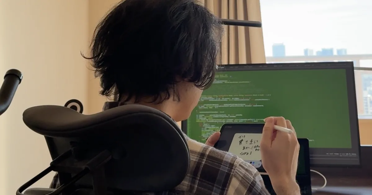 開発者の作業風景。モニターにはコードが表示され、手前では iPad に手書きで考えを書き出している
